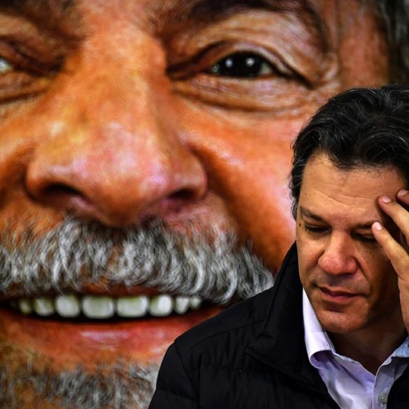 A imagem mostra Fernando Haddad cabisbaixo e um Lula atrás sorridente.